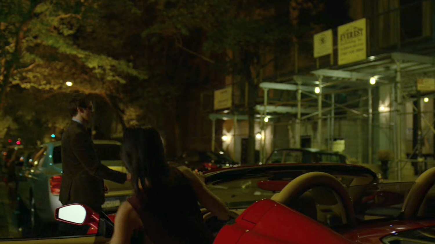 Elektra gets into a red sports car parked on the street outside faculty party.