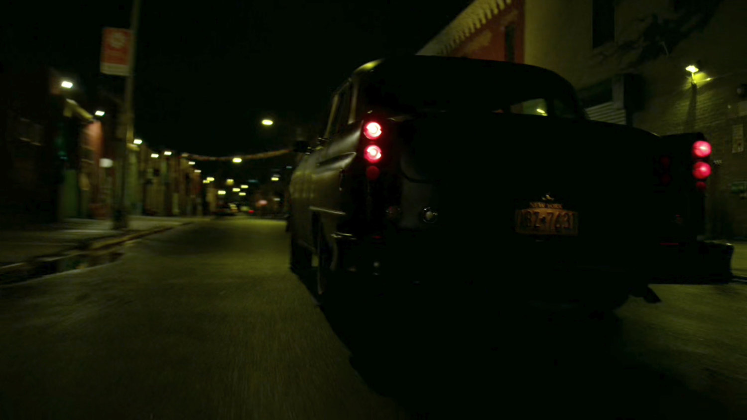 Stick's car drive down a narrow street at night.