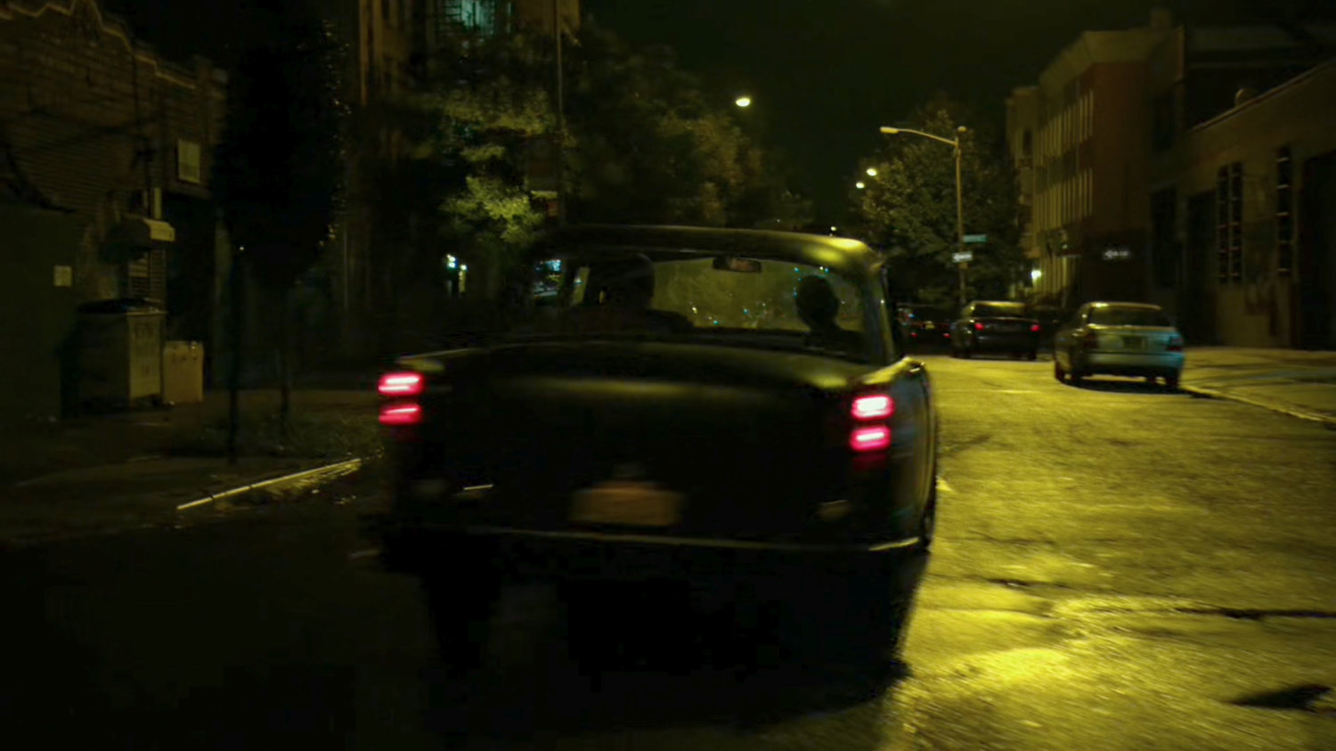 Stick's car drive down a narrow street at night.