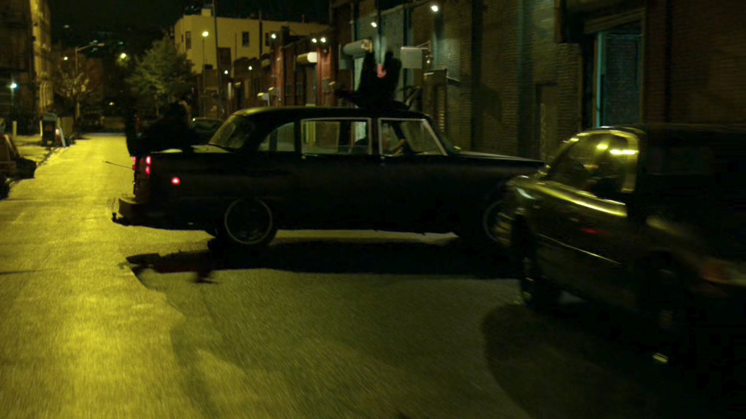 Stick's car skids sideways a narrow street at night.