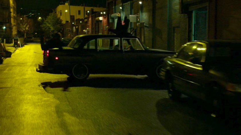 Stick's car skids sideways a narrow street at night.