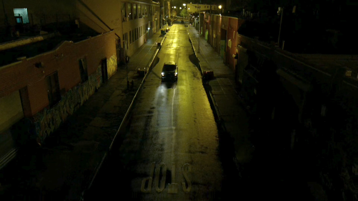 Stick's car drive down a narrow street at night.