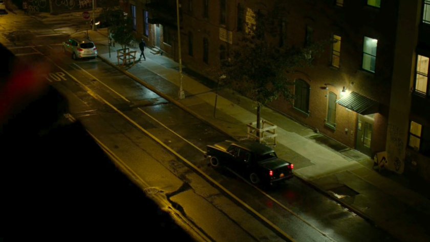 High angle of Stick's car driving away outside Matt's apartment building.