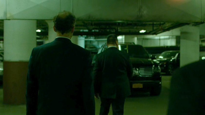 Stan Gibson escorted by bodyguards through Yakatomi parking garage.
