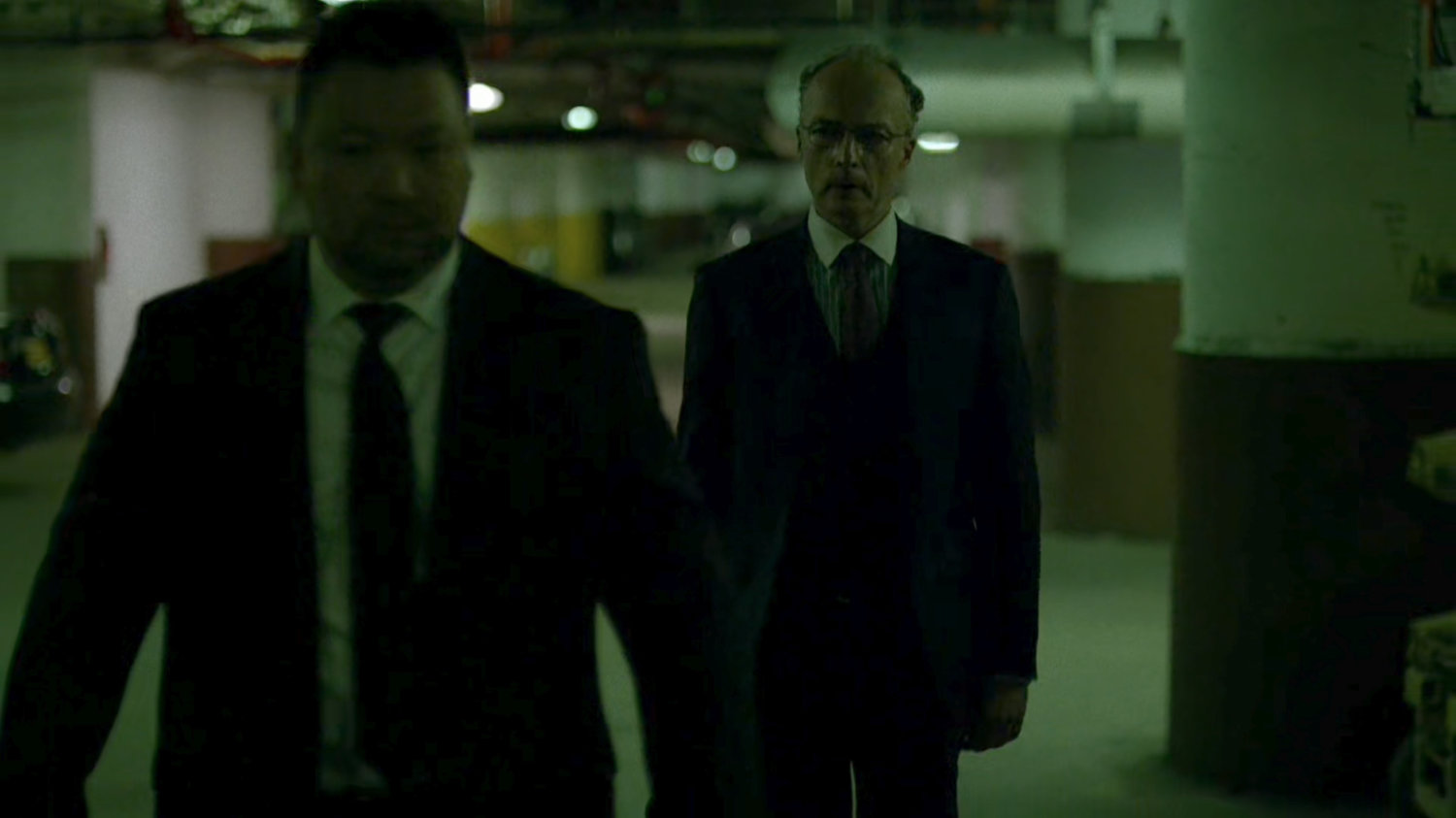 Stan Gibson escorted by bodyguards through Yakatomi parking garage.