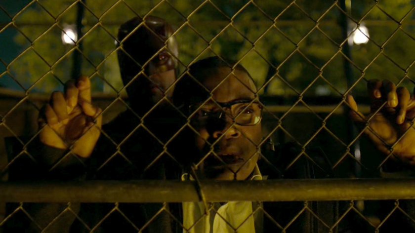 ADA Tower against a chain link fence being interrogated by Daredevil.