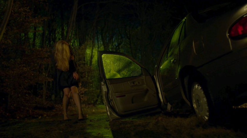 Karen stumbles from her car on a dark, wooded road.