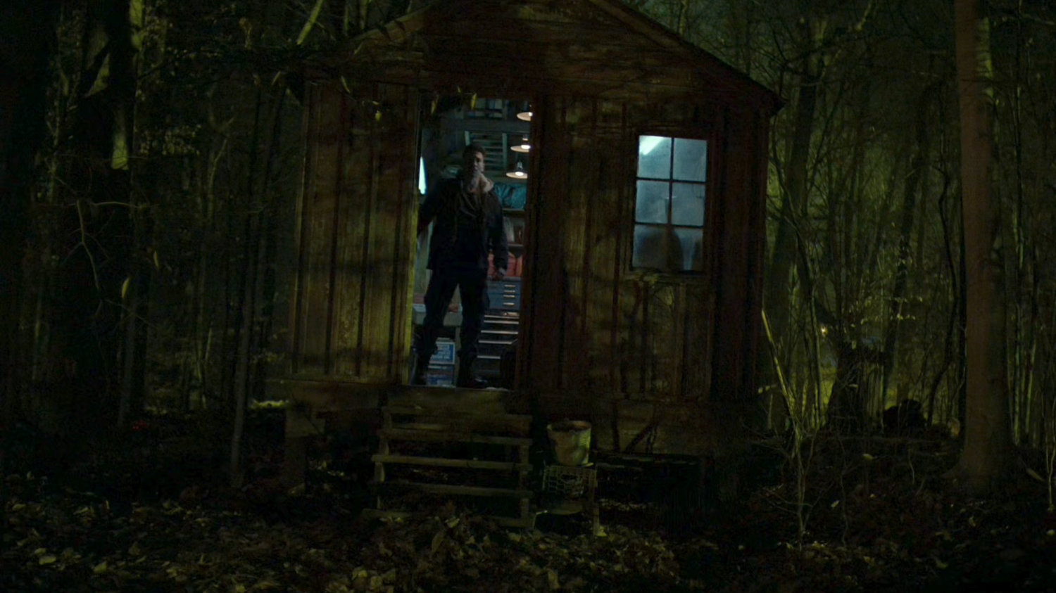 Frank standing in the doorway of a tool shed in the dark woods.