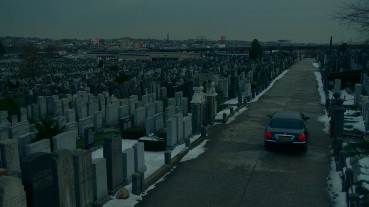 A car drives off from a snowy cemetery.
