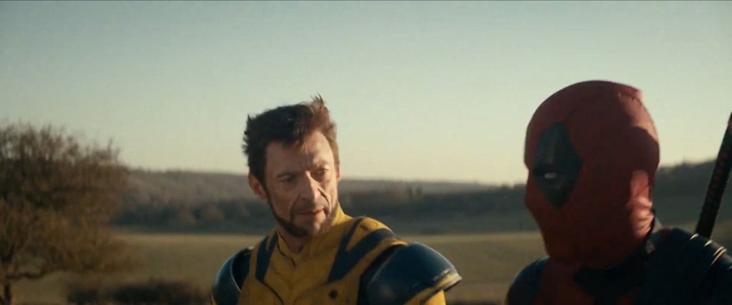 Wolverine and Deadpool walking across hilly countryside.