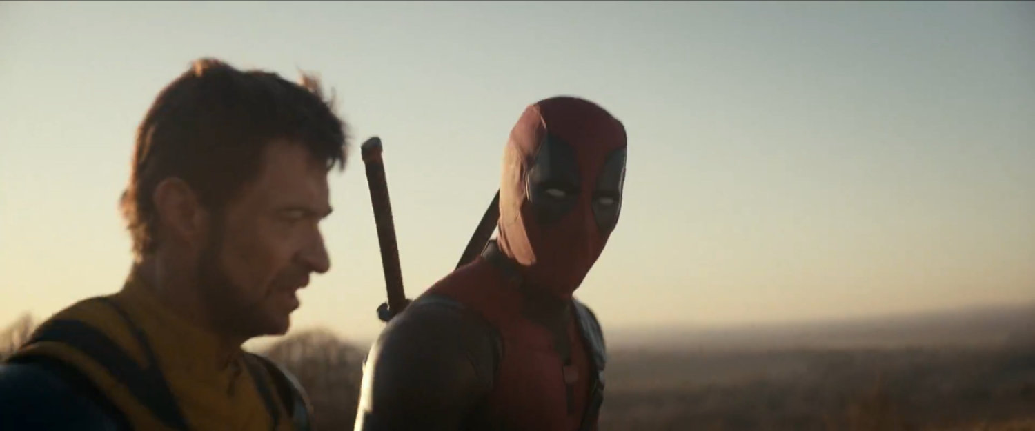 Wolverine and Deadpool walking across hilly countryside.