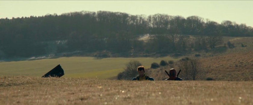 Wolverine and Deadpool walking across hilly countryside.