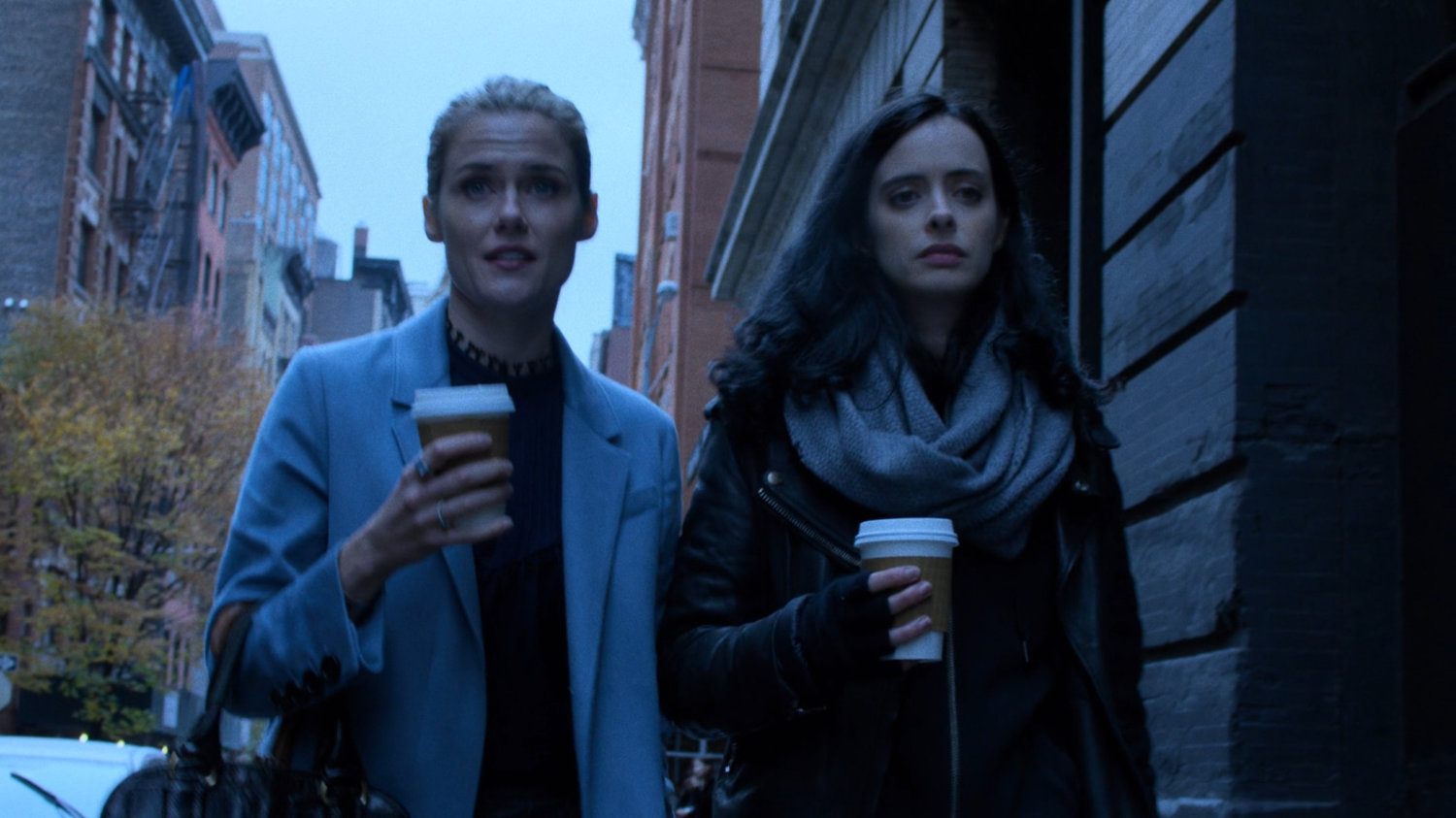 Trish and Jessica walking along sidewalk with coffee cups.
