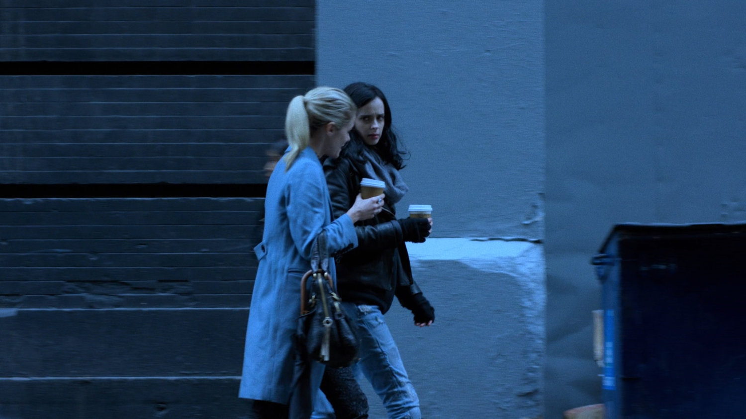 Trish and Jessica walking along sidewalk with coffee cups.