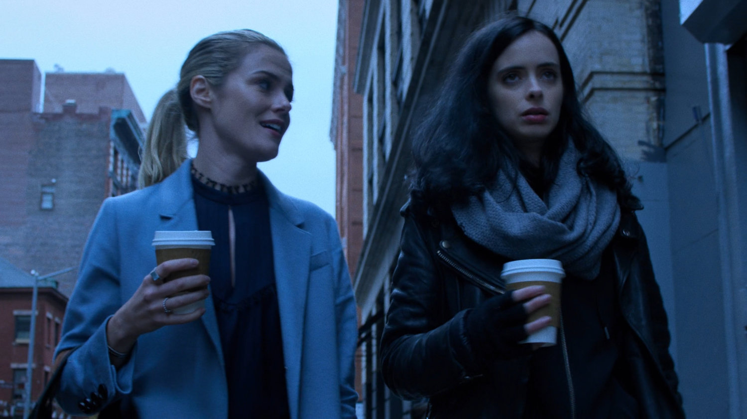 Trish and Jessica walking along sidewalk with coffee cups.