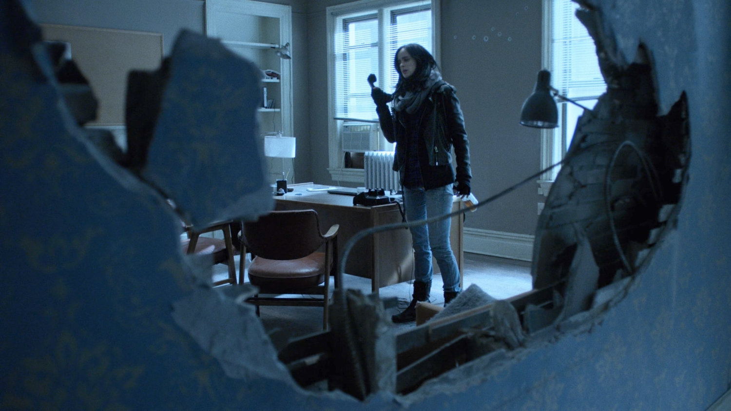 Shot looking through a hole in the wall of Alias Investigations.