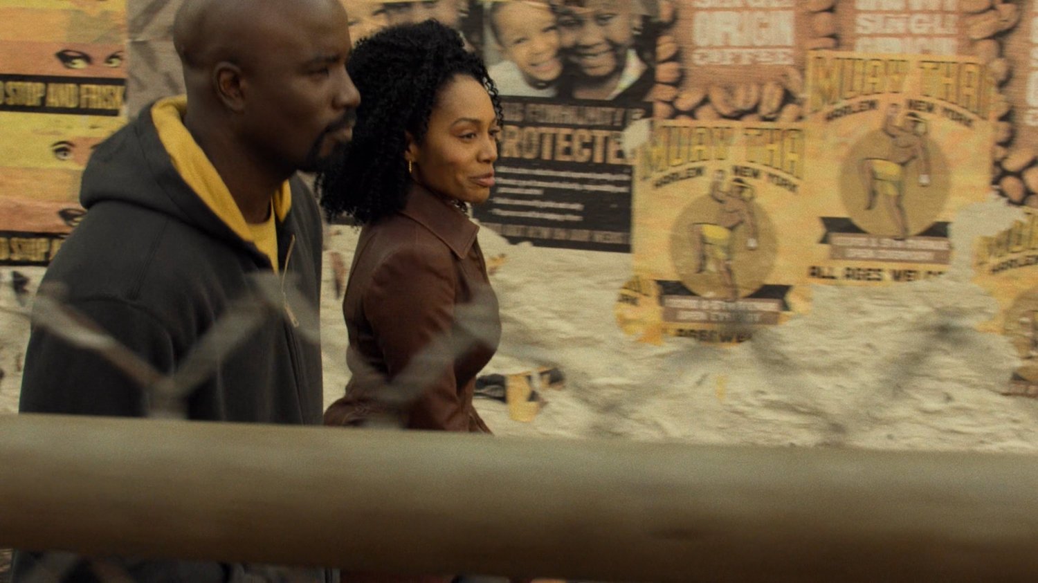 Luke and Misty walk along Harlem alley with handbills on wall.