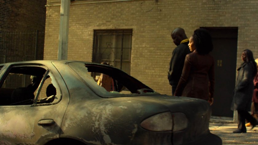 Luke and Misty walk past burned out car in Harlem.