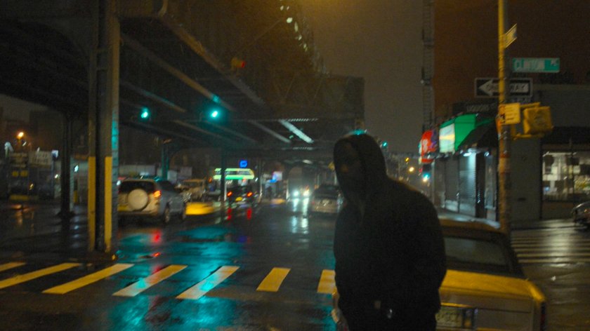 Luke crossing a rainy street by an El Train.