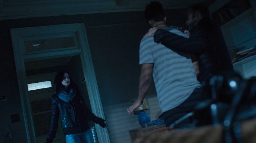 John Raymond holds Malcolm at gunpoint as Jessica stands by.