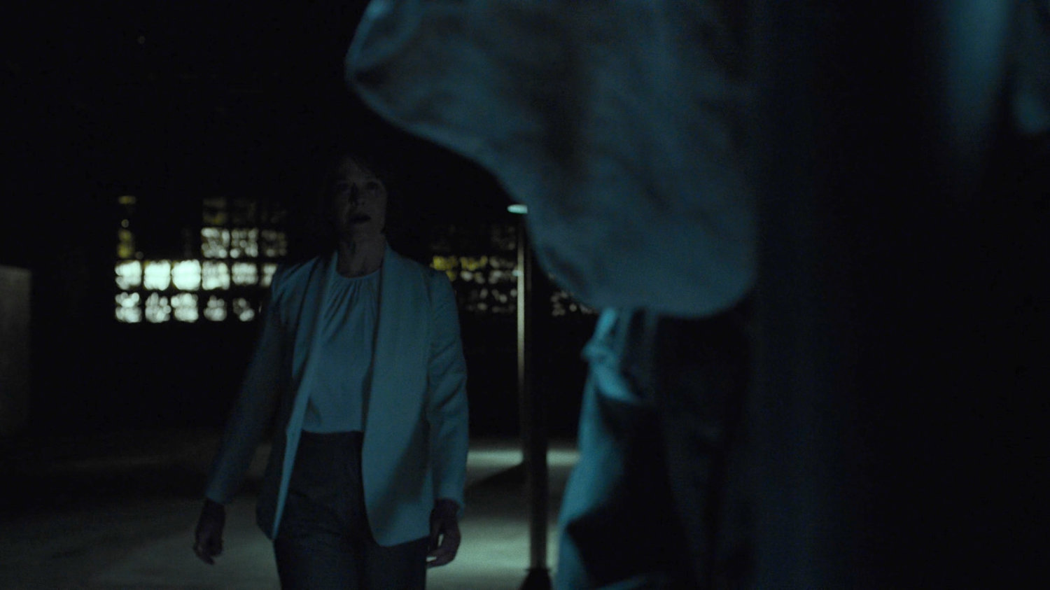 Alexandra in a dark warehouse talking to hooded prisoner.