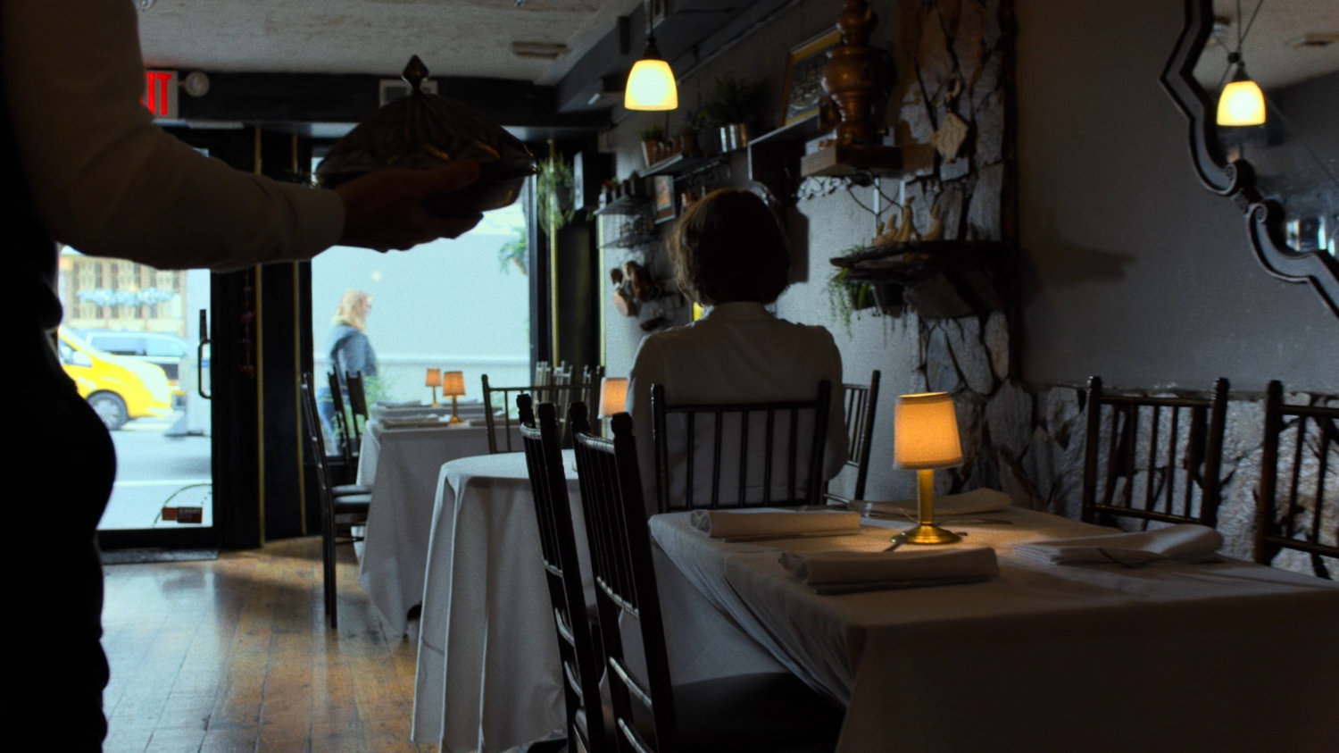 Server walking through empty Turkish restaurant towards Alexandra.