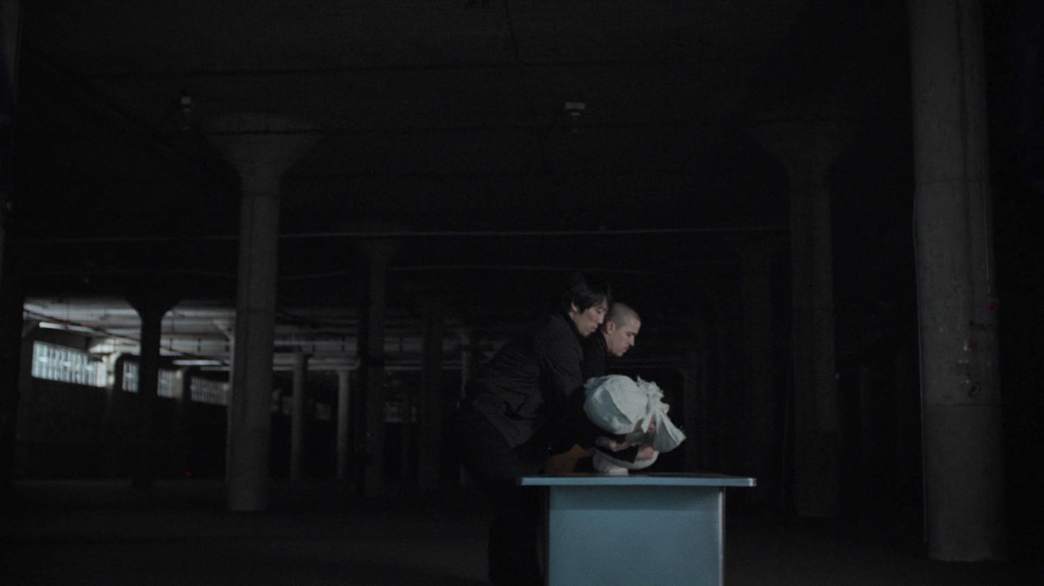 Hand members set body of Black Sky on table in dark warehouse.