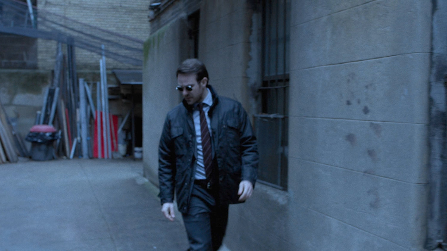 Matt listening behind him as he walk along alley.