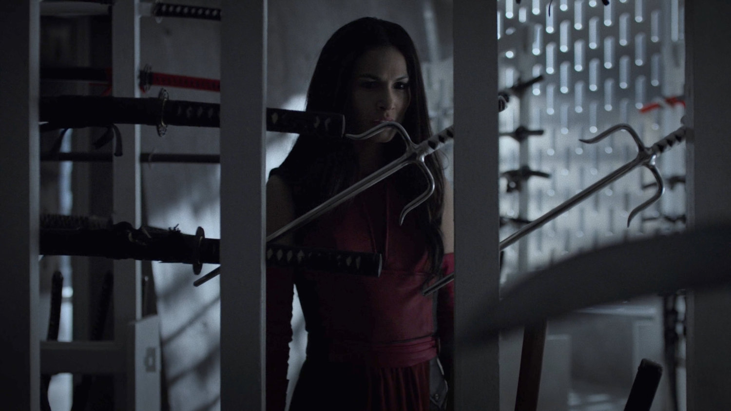 Elektra stares at racks of weapons in the Hand compound.