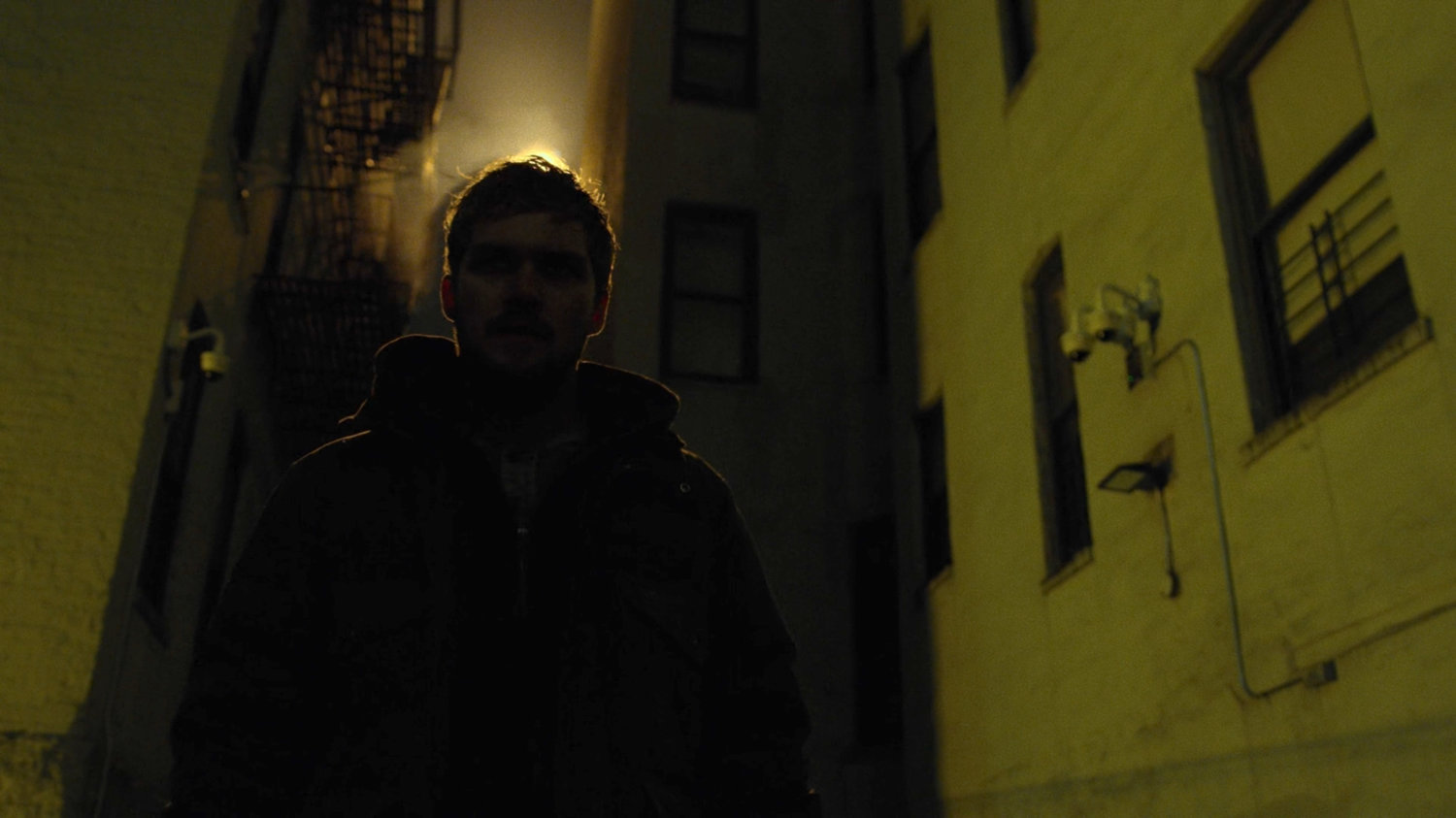 Danny walks through a backlit alley.