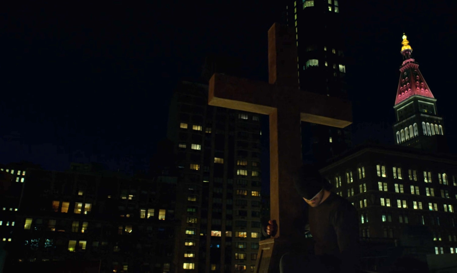 The Man in Black on a church rooftop at night, clinging to the cross.