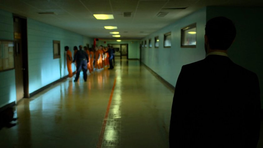 Prisoners lined up along wall in the a penitentiary hall.