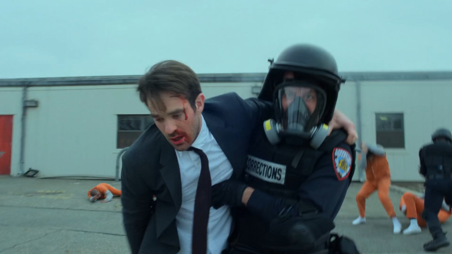 Guard leads a battered Matt past rioting inmates at penitentiary.