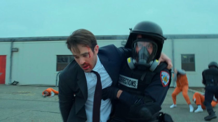 Guard leads a battered Matt past rioting inmates at penitentiary.