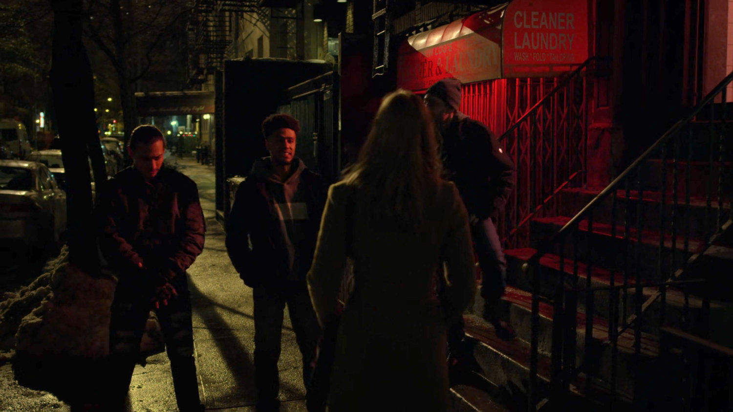 Karen confronts three youths on a dark sidewalk at night.