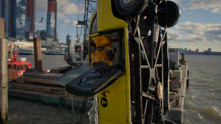 A taxi cab being pulled from the water just off a pier.