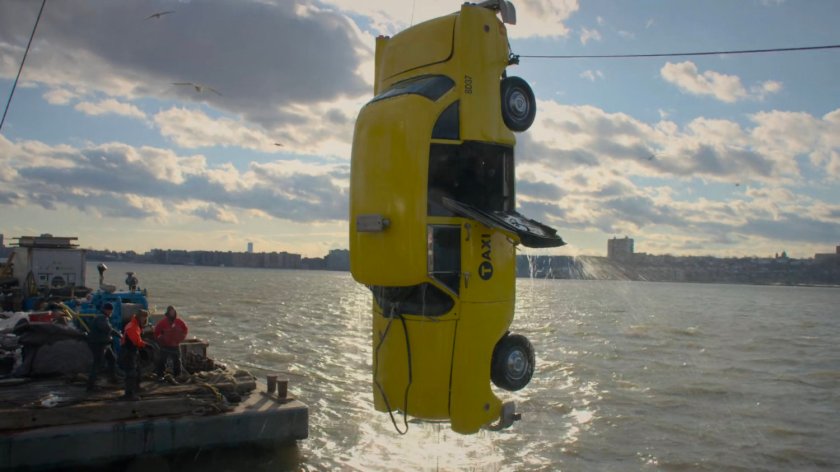 A taxi cab being pulled from the water just off a pier.