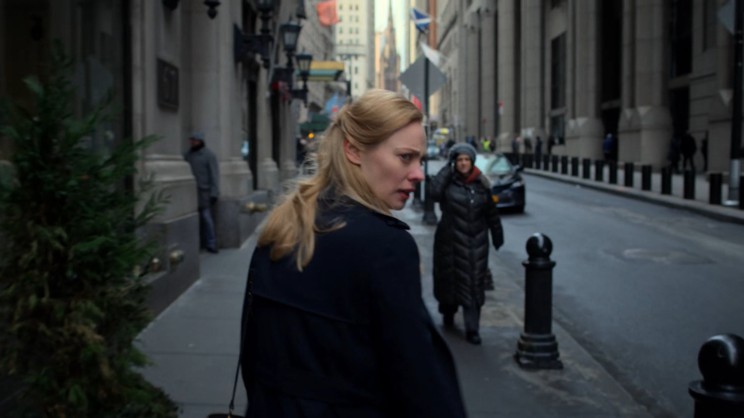 Karen looking over her shoulder on a sidewalk near Wall Street.