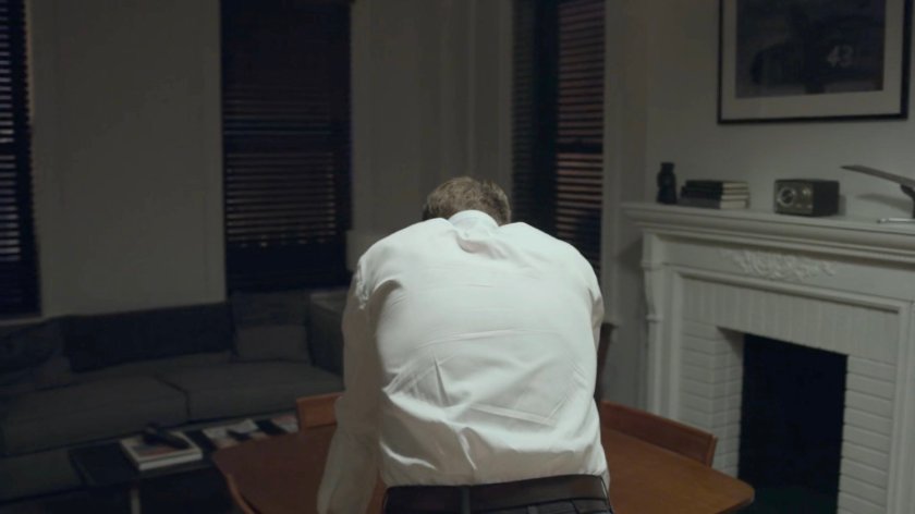 Dex leaning over the table in his apartment.