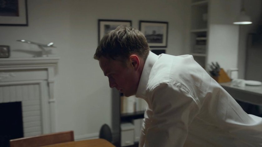 Dex leaning over the table in his apartment.
