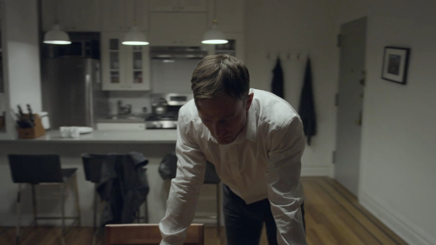 Dex leaning over the table in his apartment.