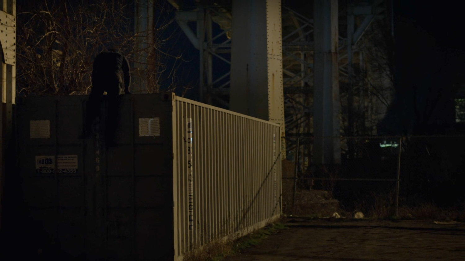Matt climbing onto a shipping container in a dark parking lot under a bridge.