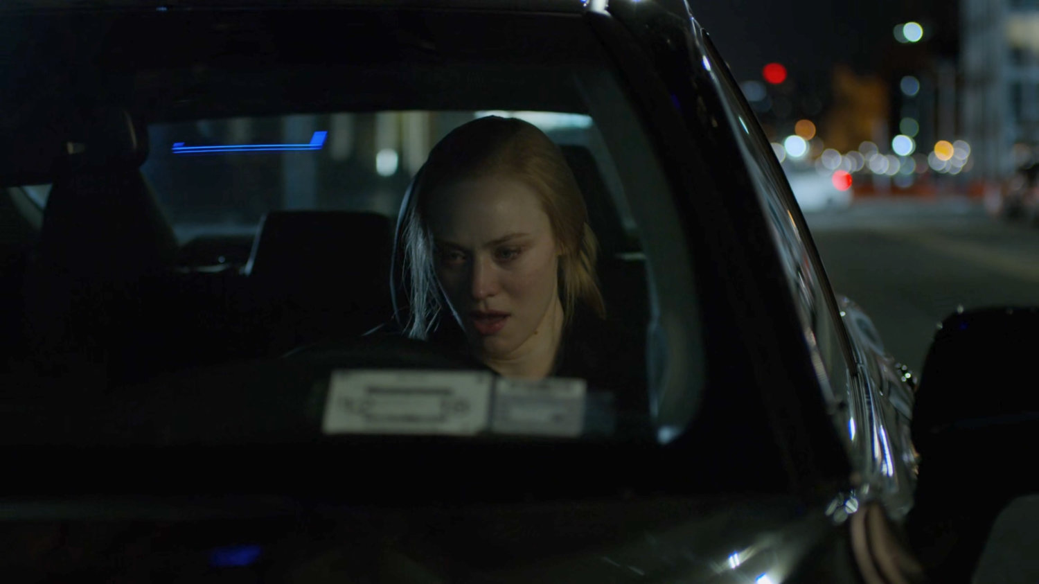 Karen sitting in her car on a street at night.