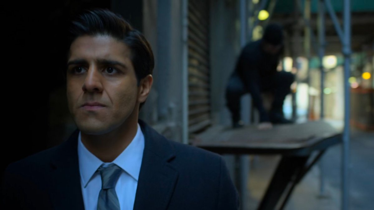 Agent Nadeem in an alley with Daredevil crouching behind him.