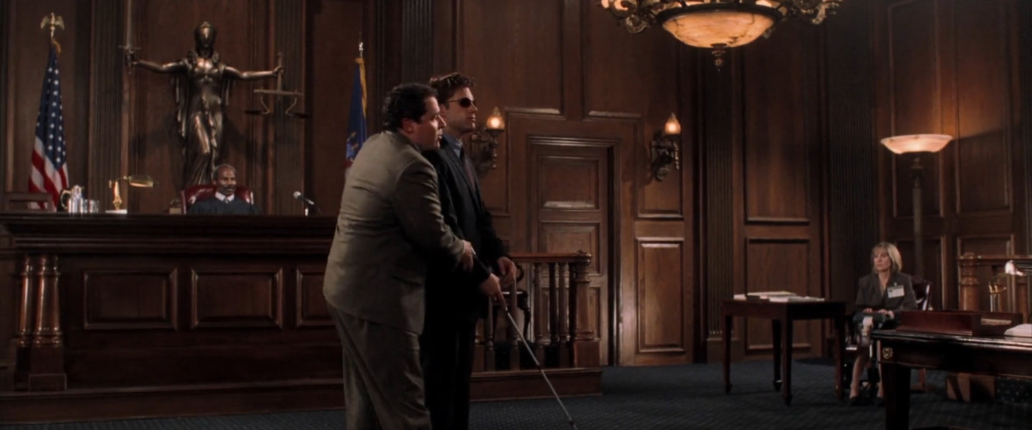 Foggy helps Matt back to his seat in a courtroom.