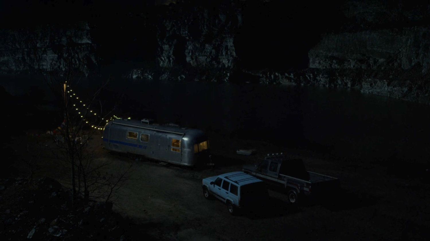 Two pickups parked at a quarry outside a silver trailer at night.