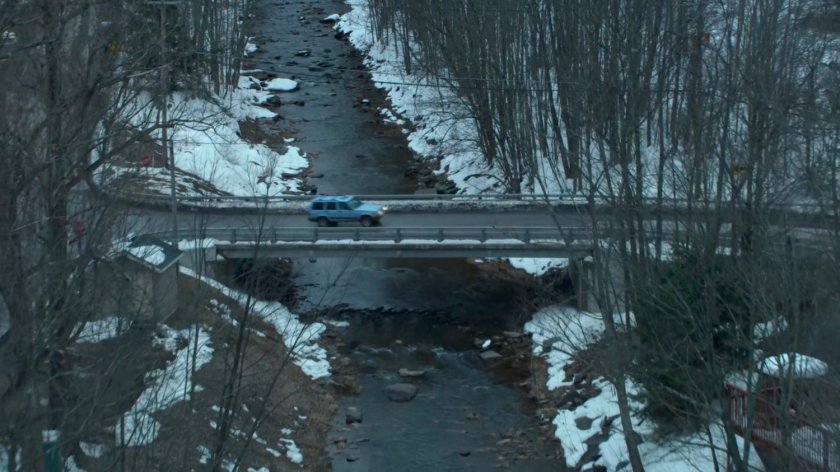 Karen's blue truck driving on a bridge crossing a river in Vermont.