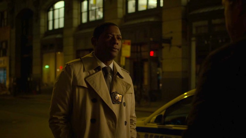 Mahoney on a dark sidewalk by a squad car.