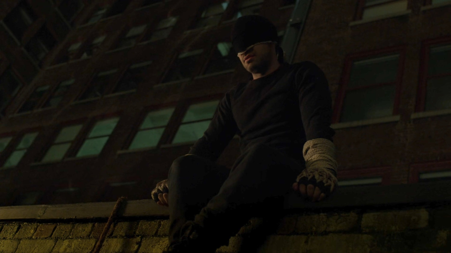 Matt sits on ledge on a dark rooftop.