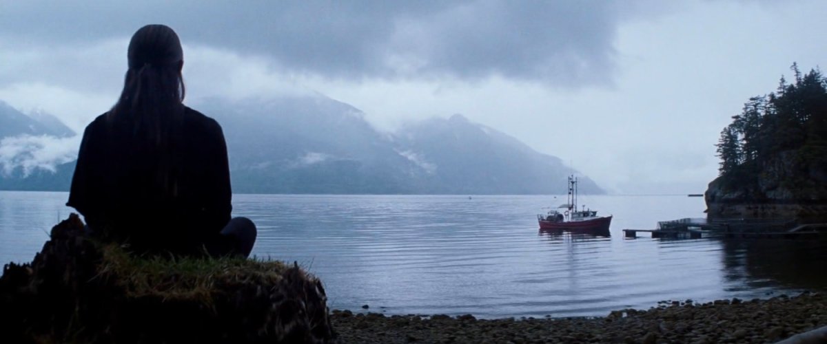 Elektra sitting on a tree stump by water.